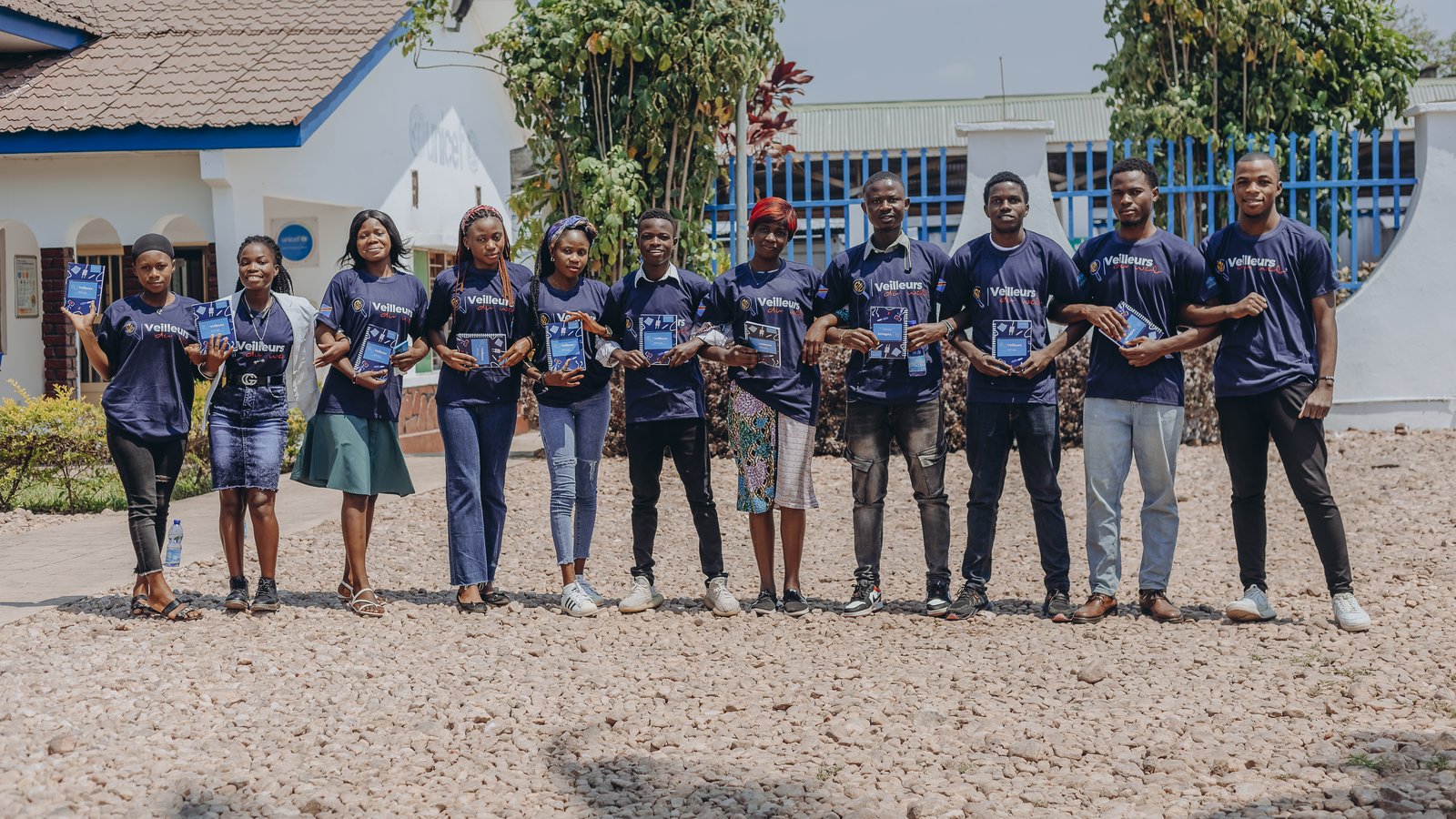 Onze Veilleurs du Web alignés devant le bâtiment UNICEF tenant leurs carnets de formation